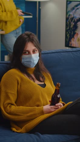 vertical video: woman relaxing with friends sitting on couch wearing face mask