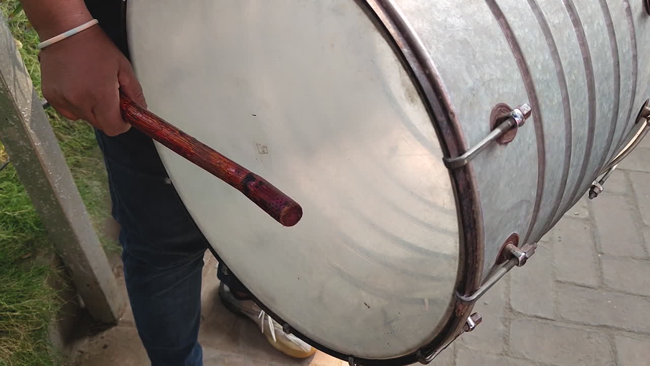 Primo piano di una persona che suona un tamburo tradizionale con una bacchetta di legno, mostrando il movimento ritmico e la superficie del tamburo