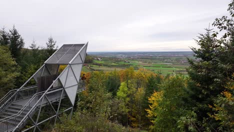 aerial shot of an observation tower in an colorful autumn forest on a mountain top with a wide and even plateu in the background