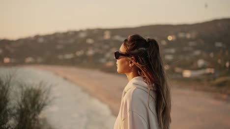 Schöne-Dame-Mit-Sonnenbrille-Geht-Bei-Kühlem-Wind-Spazieren,-Um-Den-Sonnenuntergang-Zu-Beobachten