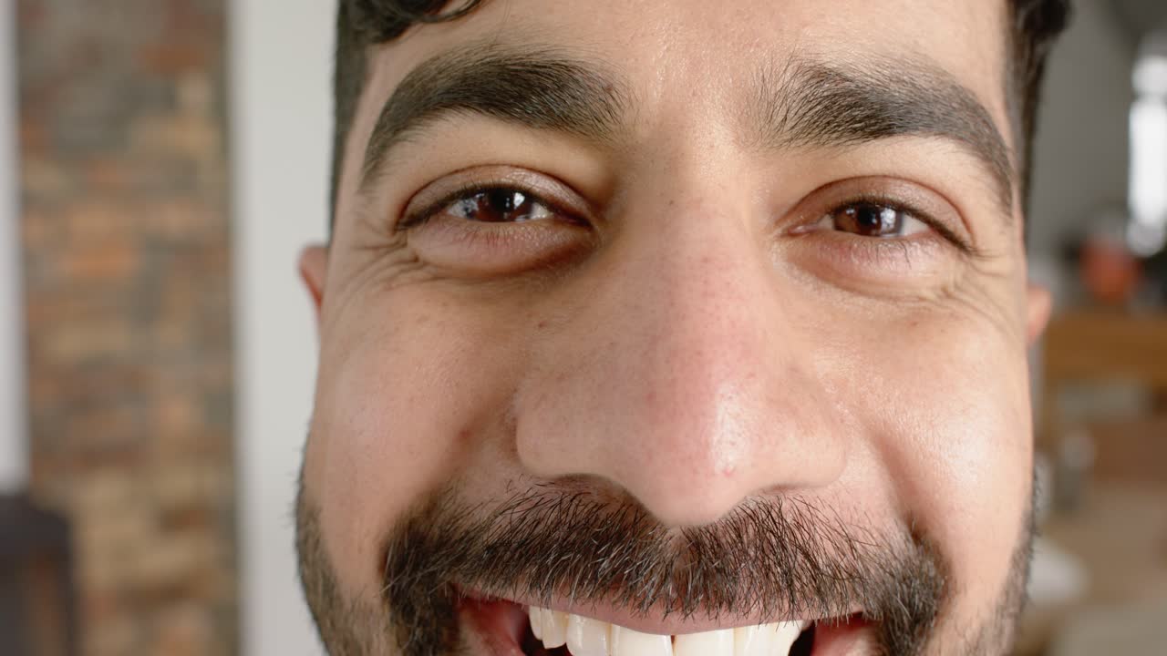 Indian man making eye contact and lifting mouth corners into broad smile expressing warmth at home