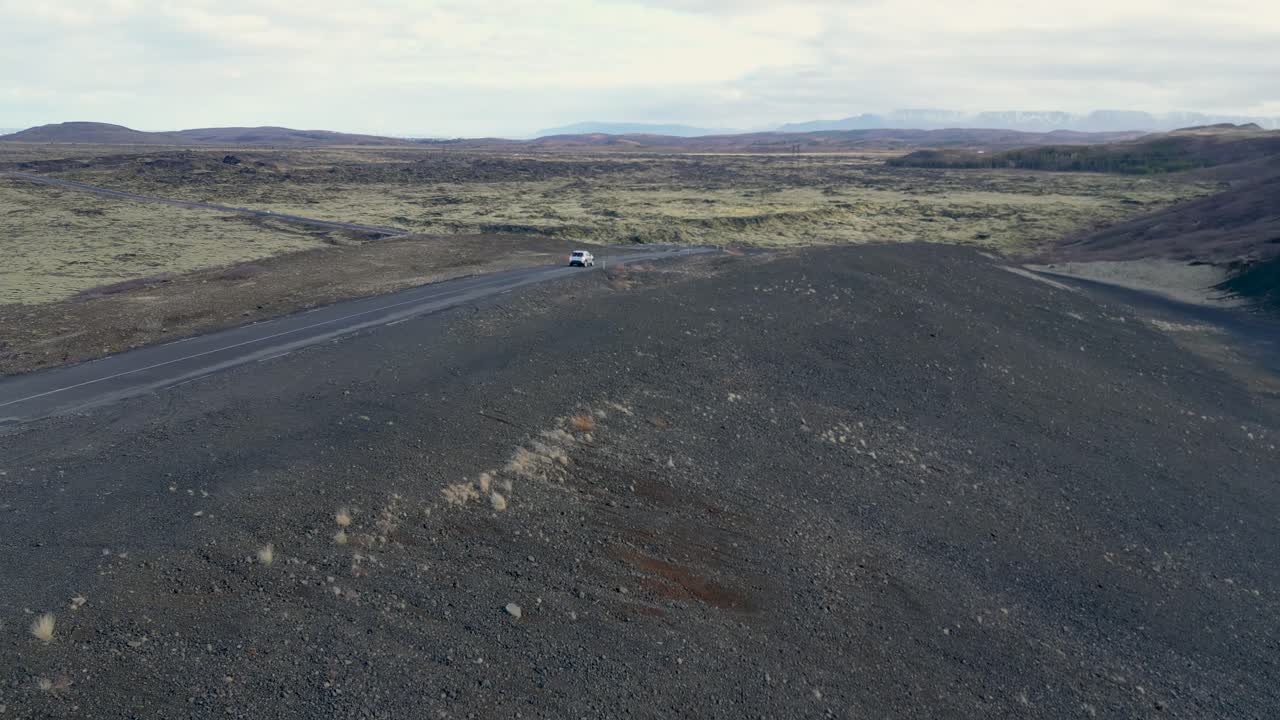 el coche conduce a través de una carretera interminable en el desierto islandés, rodeado de roca volcánica y musgo suave
