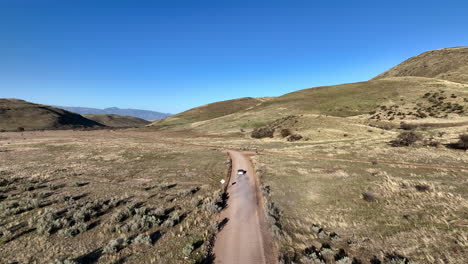 aerial shot of car driving on dirt road in willcox, arizona, epic wide drone shot with mountains in the background