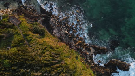 Looking-down-at-a-surfer-waiting-for-waves-along-scenic-rugged-coastal-headland-along-a-popular-surfing-holiday-spot