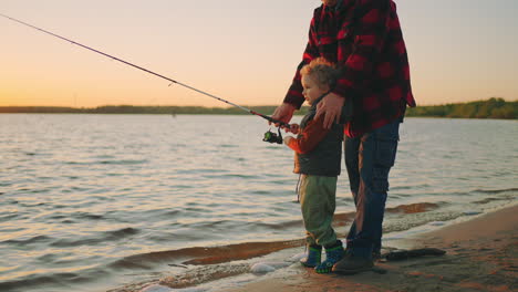 little boy is learning to catch fish trolling reels of fishing-rod happy child and father are spending weekend together