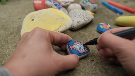 female hands drawing colorful shapes on stones with markers, point of view