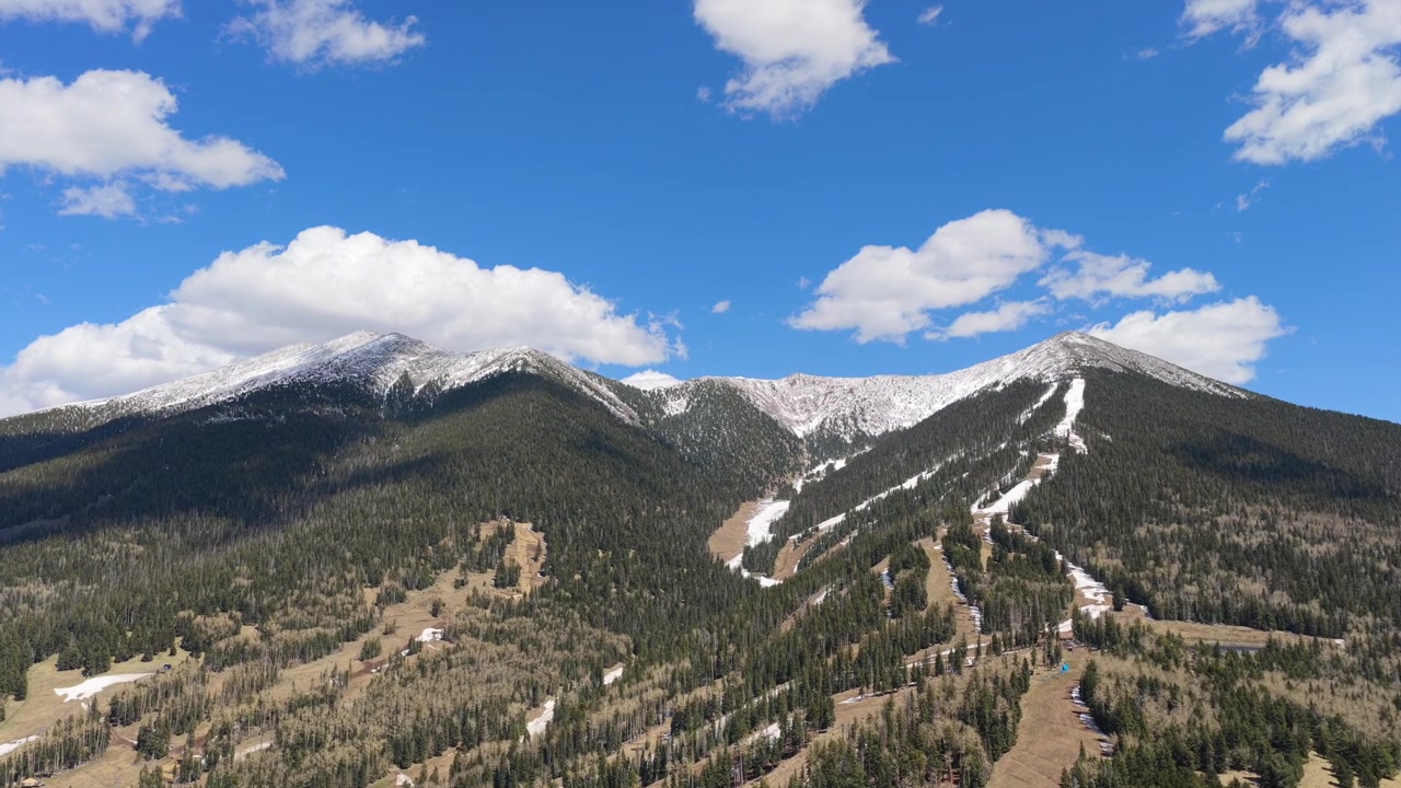 Video drone 4K che mostra una destinazione di viaggio invernale in Arizona. Viste panoramiche di pendii montani innevati, impianti di risalita attivi e una vasta distesa di pineta selvaggia sotto un sole invernale splendente