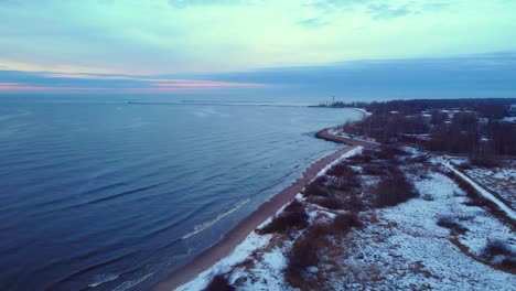 Impresionante-Toma-Aérea-De-Drones-De-La-Playa-Cubierta-De-Nieve-En-Letonia,-Puesta-De-Sol