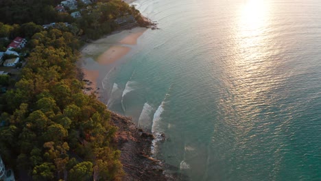 drone footage of a quiet small beach surrounded by forest basking i nthe afternoon sun near noosa, sunshine coast, australia