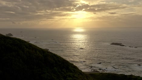 Aerial-Cinematic-Shot-Flying-Over-Lush-Forested-Coastline-Of-Chiloe-Island-With-Golden-Sunset-On-The-Horizon