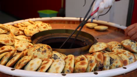 seller taking shaobings from a tandoori oven with tweezers