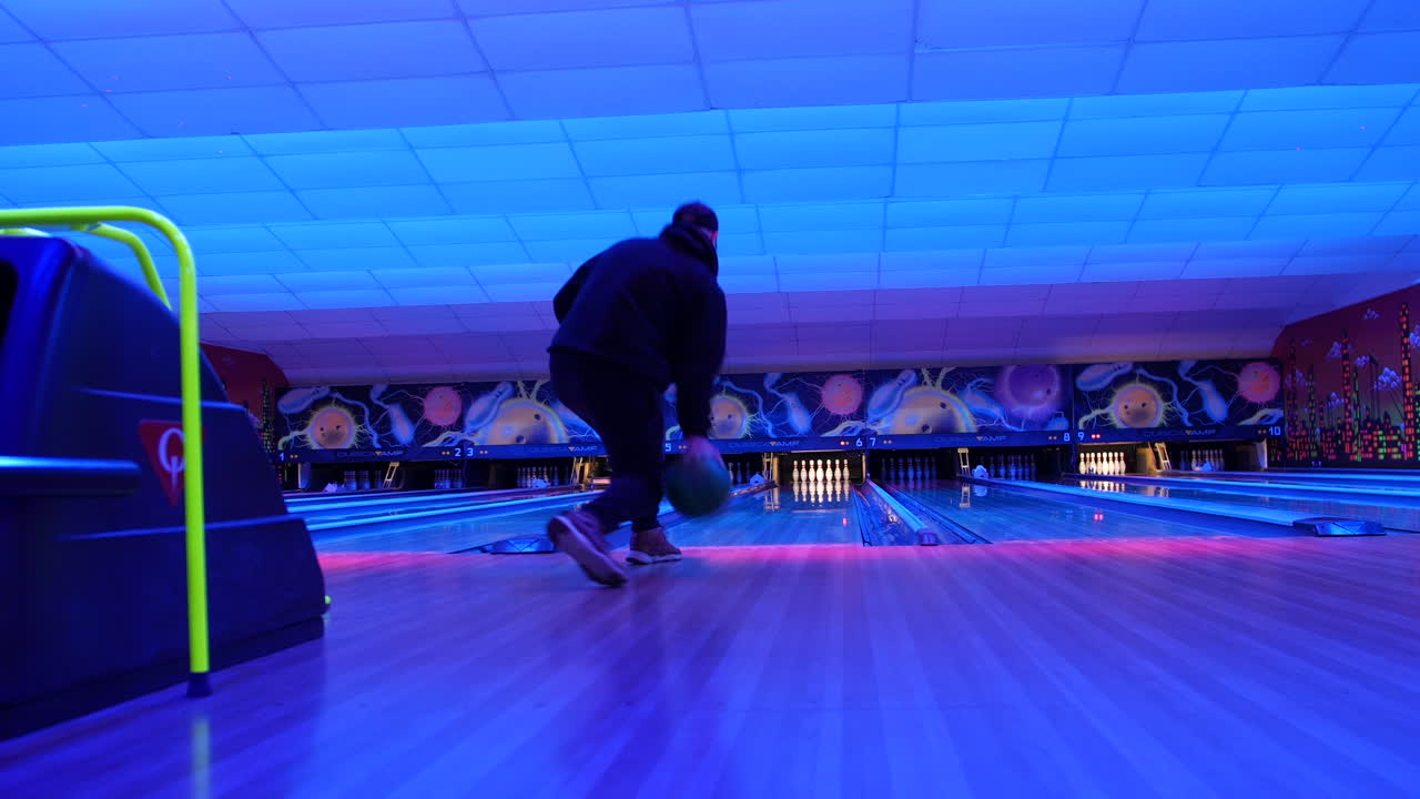 A bowler releasing the ball down a neon-lit lane in a vibrant bowling alley. The illuminated pins and dynamic atmosphere set the stage for a strike