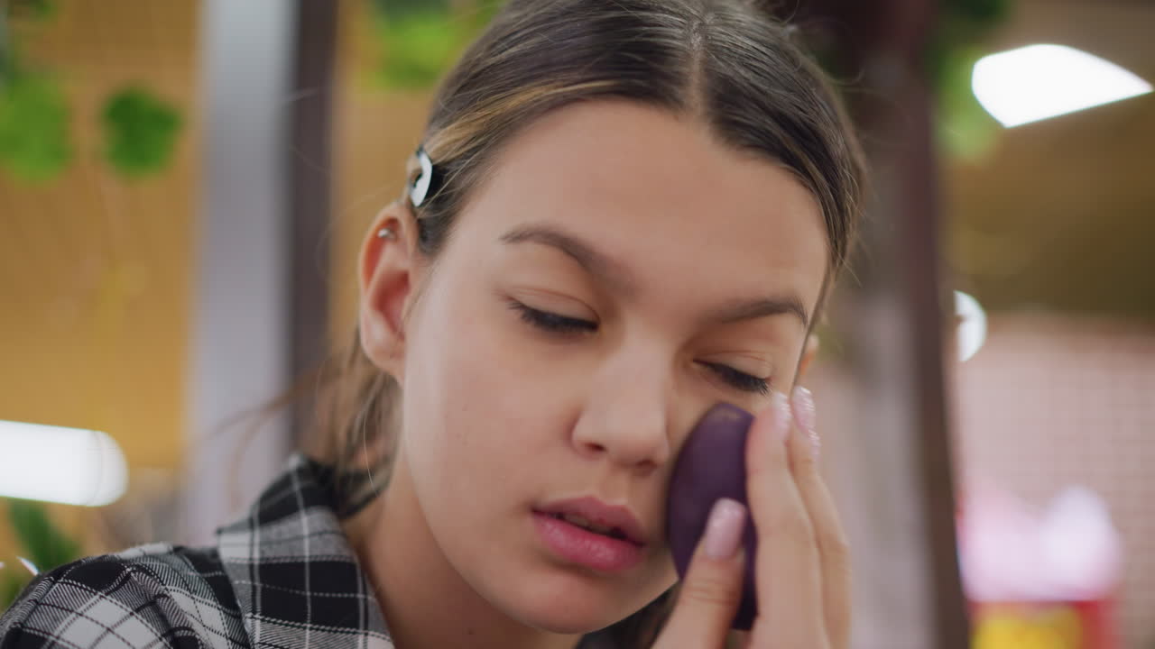 Young girl carefully blending makeup on jaw and cheeks using beauty sponge, smooth application enhances natural beauty, creating flawless complexion with precision, soft lighting