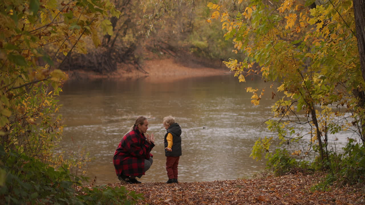 colores brillantes de principios de otoño en el bosque mujer y niño pequeño están descansando juntos en la orilla del lago en el bosque jugando con hojas divirtiéndose los fines de semana