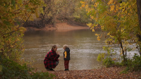 Helle-Farben-Des-Frühen-Herbstes-Im-Wald.-Frau-Und-Kleiner-Junge-Ruhen-Sich-Zusammen-Am-Ufer-Eines-Sees-Im-Wald-Aus,-Spielen-Mit-Blättern-Und-Haben-Am-Wochenende-Spaß