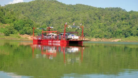 Shot-of-a-red-ferry-boat-sailing-out-with-cars-on-deck-in-Pak-Nai-fisherman-village,-Nan-province,-Thailand-on-a-sunny-day