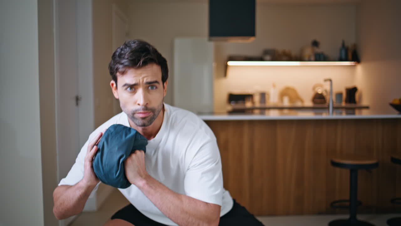 Focused sportsman performing squats holding weighted bag at home workout closeup