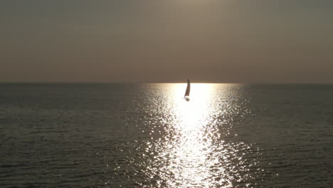 Eine-Schwenkende-Luftaufnahme-Eines-Segelboots-Auf-Einem-See-Bei-Sonnenuntergang