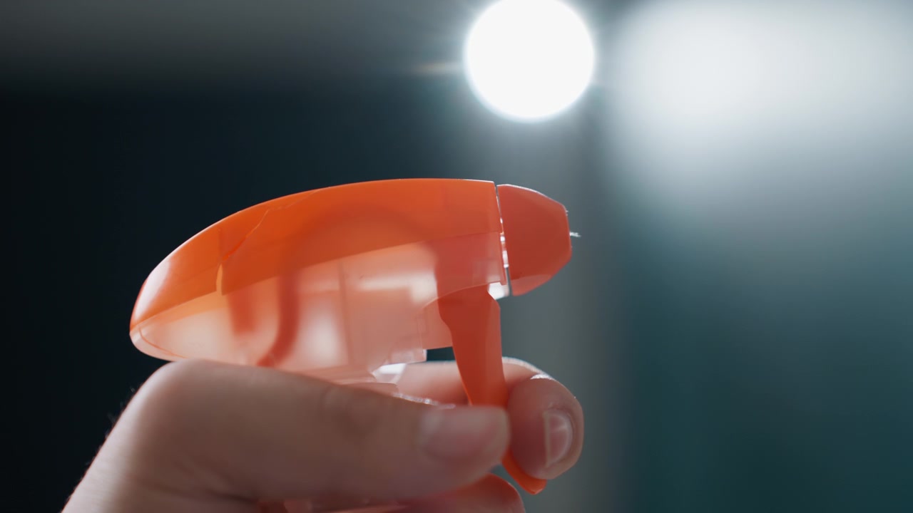 Spruzzo retroilluminato che rivela goccioline scintillanti su sfondo scuro, dimostratore di prodotto che testa un detergente per la casa, illuminazione da studio cinematografica, bokeh ad alto contrasto, nebbia scintillante, spot pubblicitario drammatico.