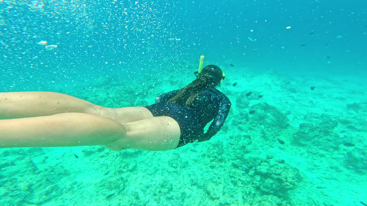Joven buceando bajo el agua rodeada de burbujas y peces en un mar turquesa