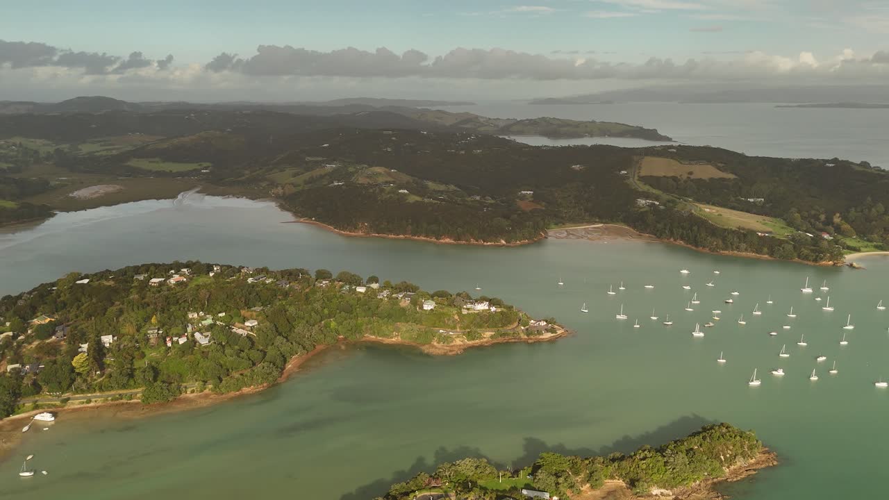 Aerial panorama showing sailboats and yachts anchored in the clear turquoise waters of Shelly Beach in the Surfdale area of Waiheke Island, New Zealand.