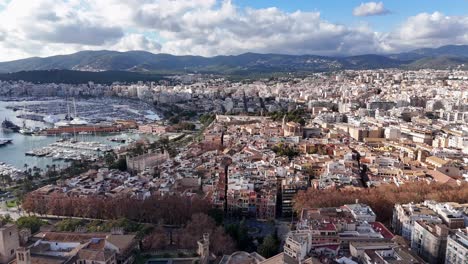 aerial establishing shot showing beautiful historic city of palma de mallorca with harbor and sailing boats - mountain range of island in background - spanish neighborhood in capital