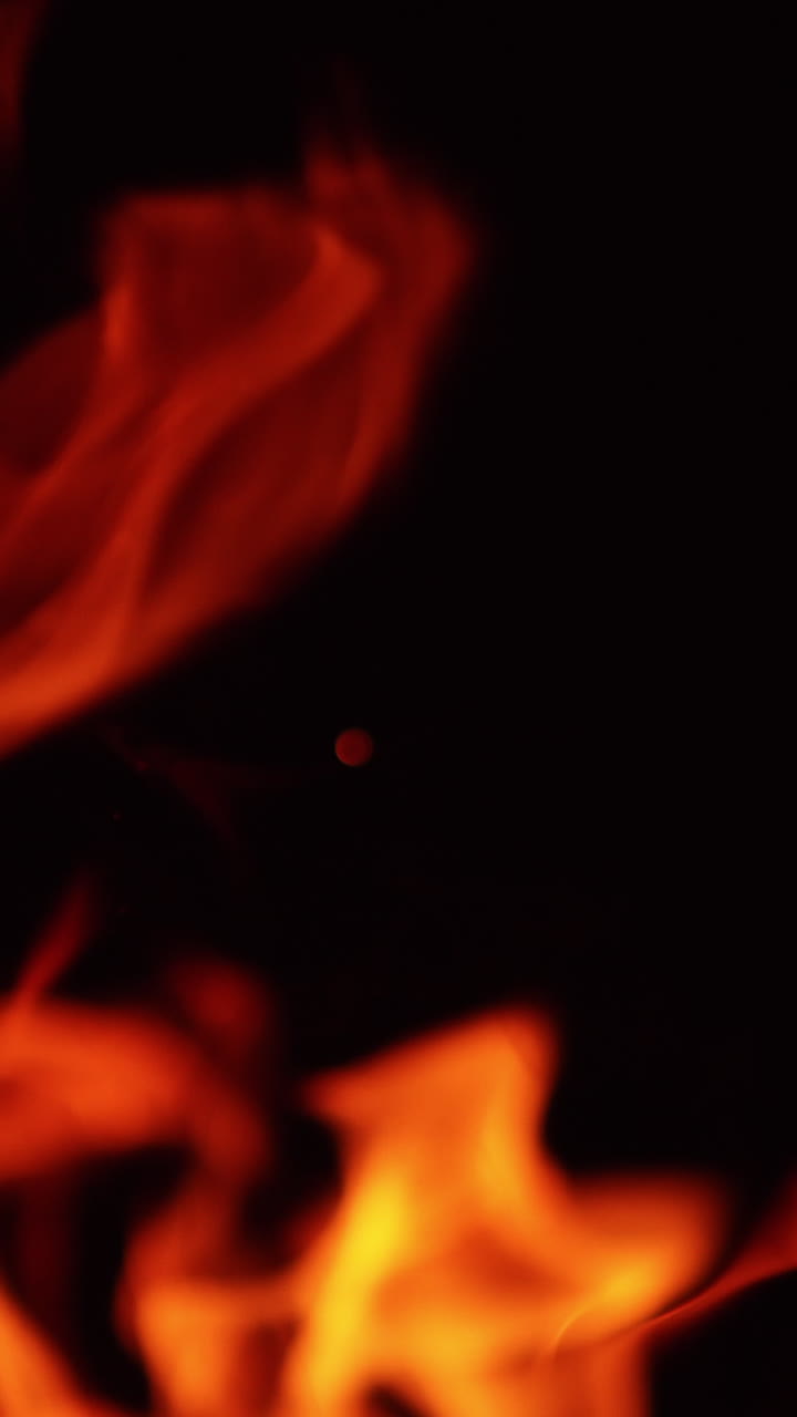 Tongues of red and yellow flame moving in the darkness. Tiny sparks fly up into the air. Close up. Vertical video