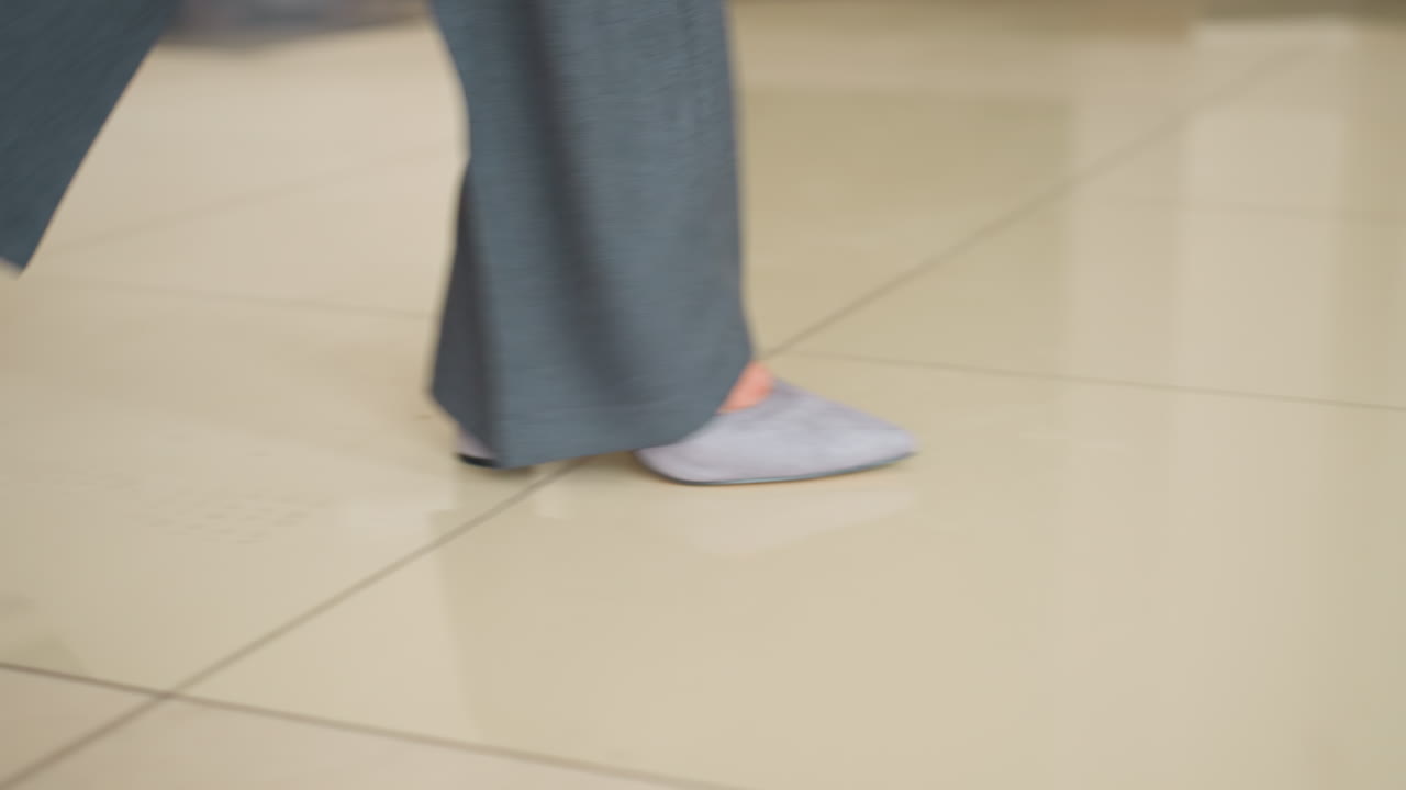 Motion-blurred close-up of business professional walking in gray formal trousers and light socks across corporate office floor. Dynamic movement shows confident stride over beige