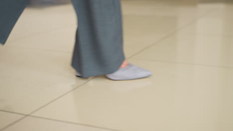 motion-blurred close-up of business professional walking in gray formal trousers and light socks across corporate office floor. dynamic movement shows confident stride over beige