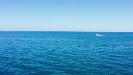 Barco-Blanco-En-El-Mar-Mediterráneo-Pasando-Vista-Aérea-Agua-Azul