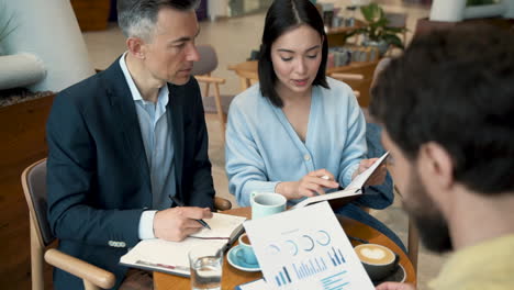 a work team analyzing and comparing papers and results in a meeting in a coffee shop