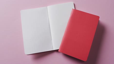 close up of open blank book and red closed book with copy space on pink background in slow motion