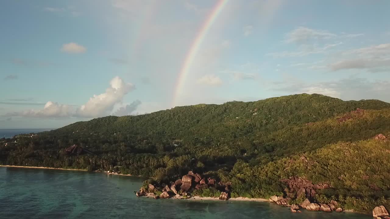 Opening drone shot of the rainbow behind the mountains of La Digue island on Seyshelles. Beach Source D'Argent.