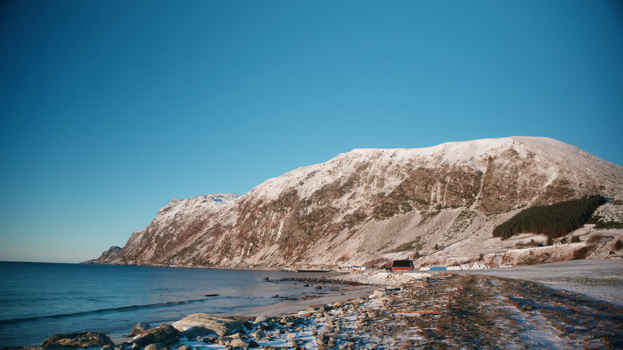 Naturskønt billede af et snedækket landskab med en lille strand, hvor solen skinner klart på landskabet på en kold vinterdag i Norge