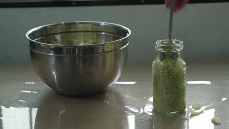 person transferring thinly sliced cabbage into glass container with a spoon. - closeup shot