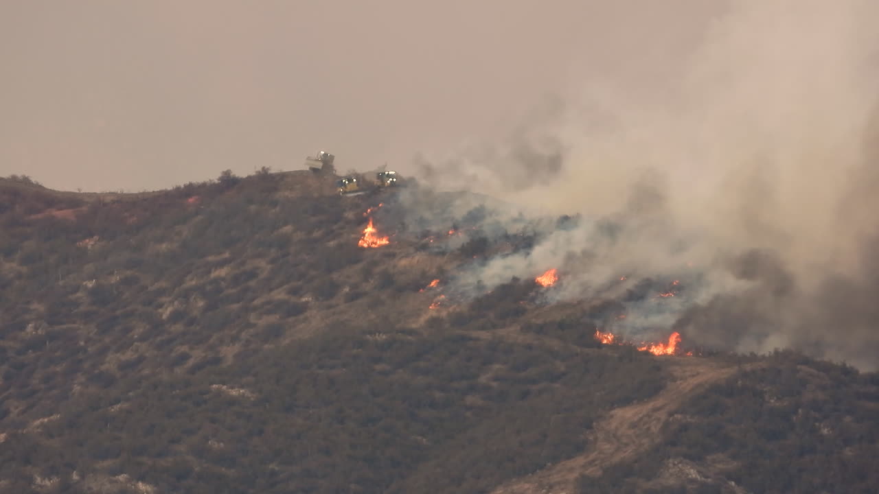Il fumo si innalza da un incendio su una collina boscosa in California, vista ampia e statica