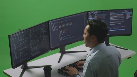 side view of asian man developer having backache while write code with multiple computer screens in green screen studio