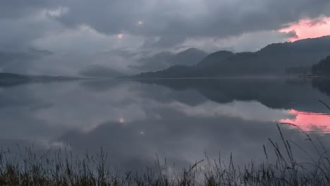 Low-clouds-crawl-over-the-dramatic-sunset-sky-above-the-still-mirrorlike-lake