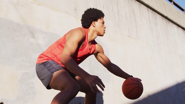 Fitter afroamerikanischer Mann treibt Sport im Freien in der Stadt und prellt einen Basketball.