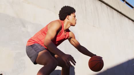 fit african american man exercising outdoors in city, bouncing basketball