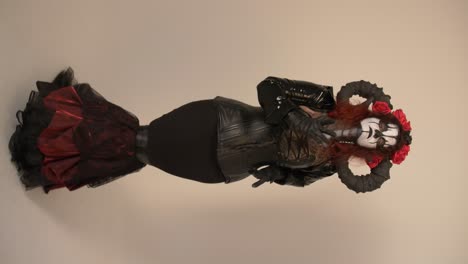catrina cosplay girl looking around and  moving her hands to the camera with domina outfit and dark background, full shot
