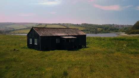 Drohnenaufnahme-über-Einem-Haus-Auf-Einem-Feld,-Um-Einen-See-Dahinter-Freizulegen