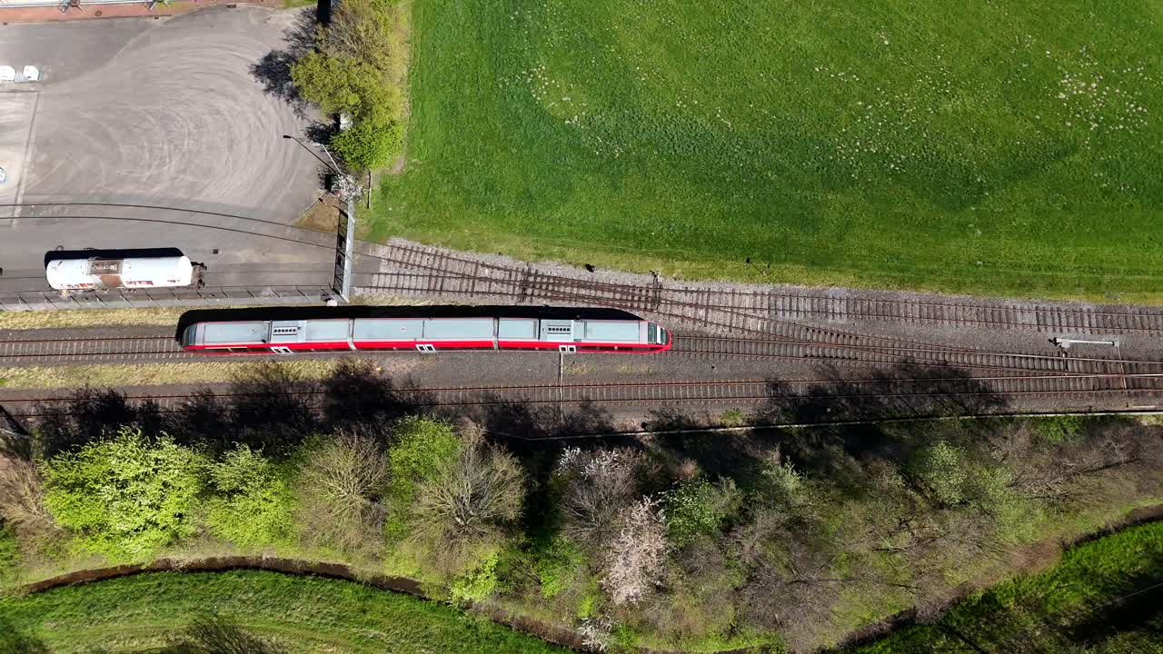 Red train on railway tracks in rural area in america. Sunny day in summer. Green Grass and trees. Aerial top down tracking shot.