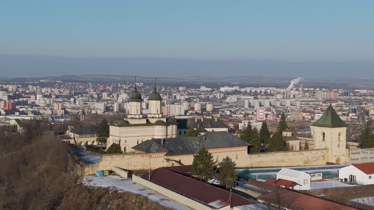 Vista aérea de drone do Mosteiro de Cetățuia, um local histórico em Iași, Romênia, com cúpulas verdes com vista para os telhados cobertos de neve da cidade e para o horizonte urbano.