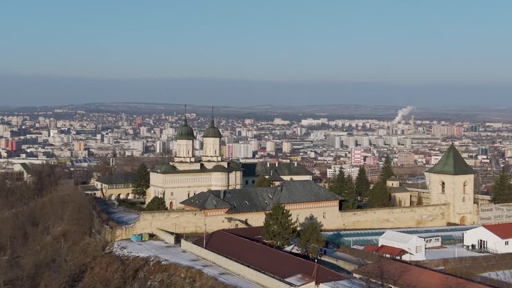 Vista aérea de drone do Mosteiro de Cetățuia, um local histórico em Iași, Romênia, com cúpulas verdes com vista para os telhados cobertos de neve da cidade e para o horizonte urbano.