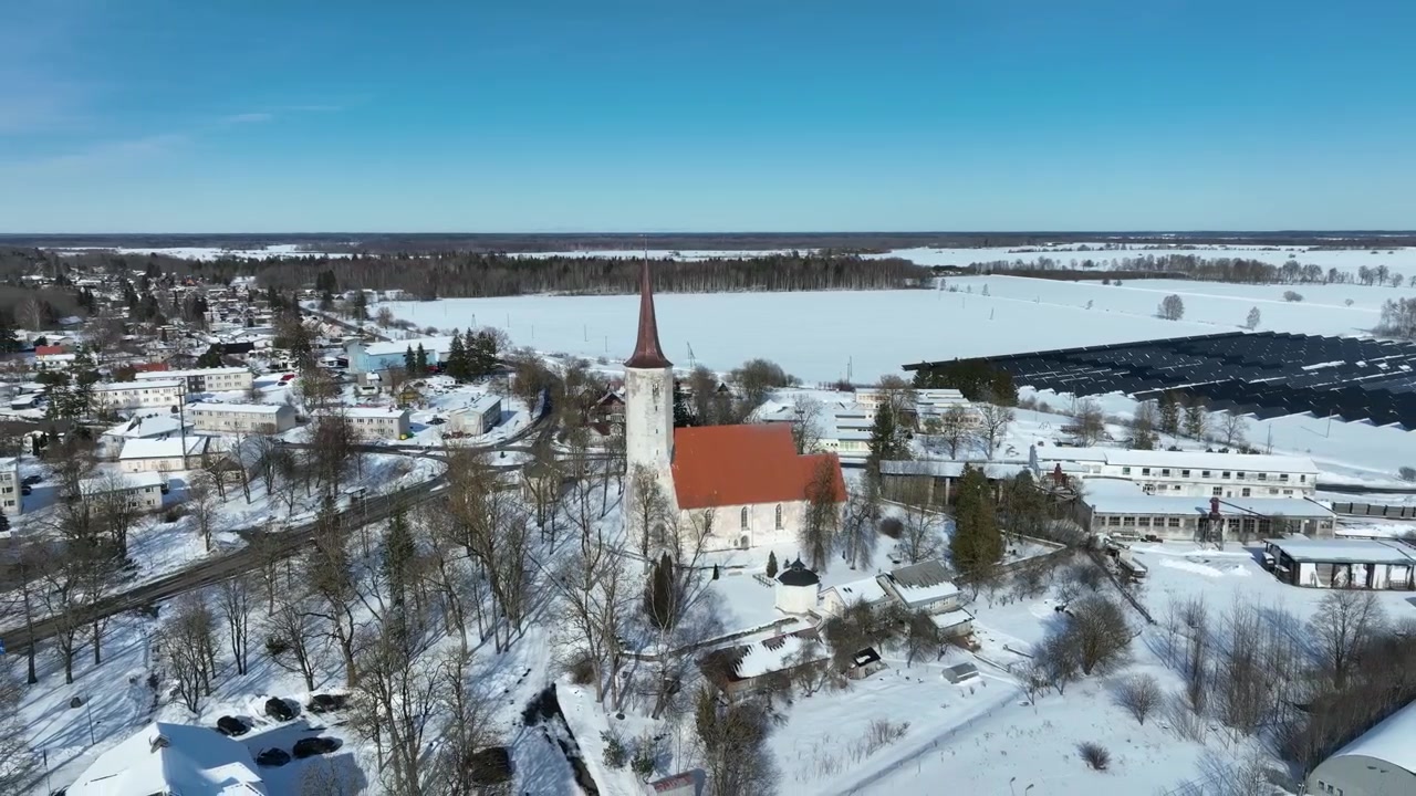 Flygfoto som zoomar ut över S:t Mauritius (S:t Maurice) kyrka i Haljala, med solkraftverk i bakgrunden. Estland