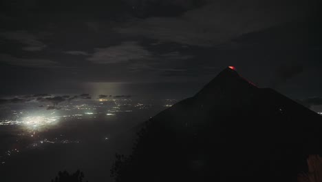 fuego volcano erupting at night with glowing lava and city lights bellow, night time lapse