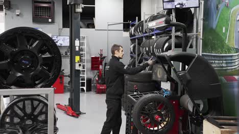 técnico de taller de neumáticos que usa una máquina de equilibrador de ruedas automáticas para reparar la rueda
