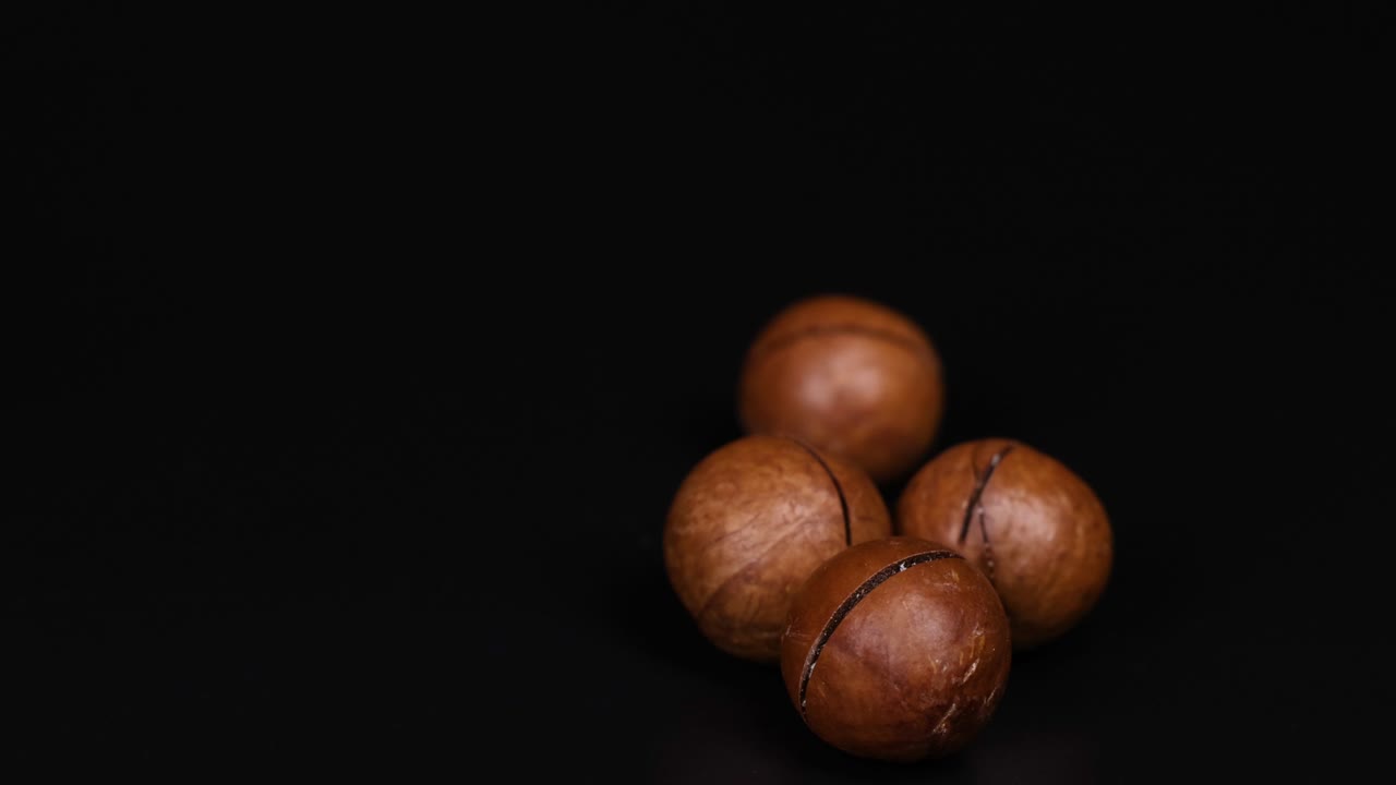 Noci di macadamia che ruotano fluidamente su una superficie nera