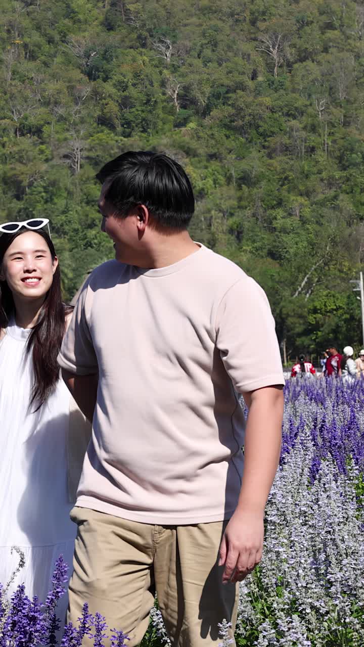 Sepasang kekasih yang bahagia berjalan melintasi ladang lavender yang mekar di bawah sinar matahari cerah di Thailand.